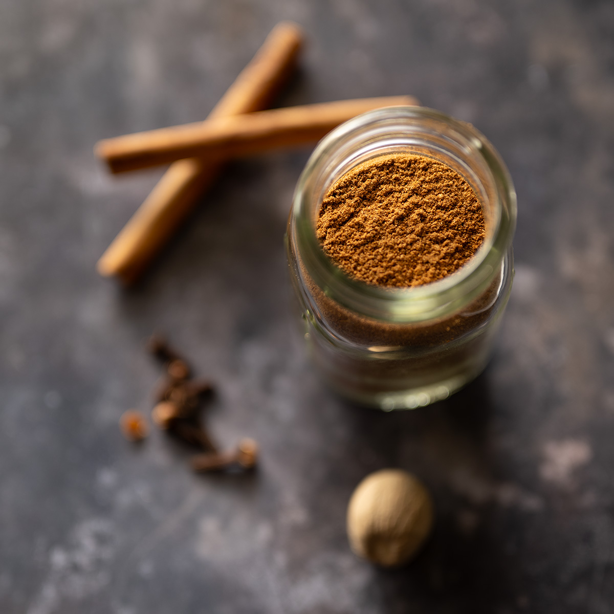 Irish mixed spice in a jar with cinnamon sticks, whole nutmeg, and whole cloves